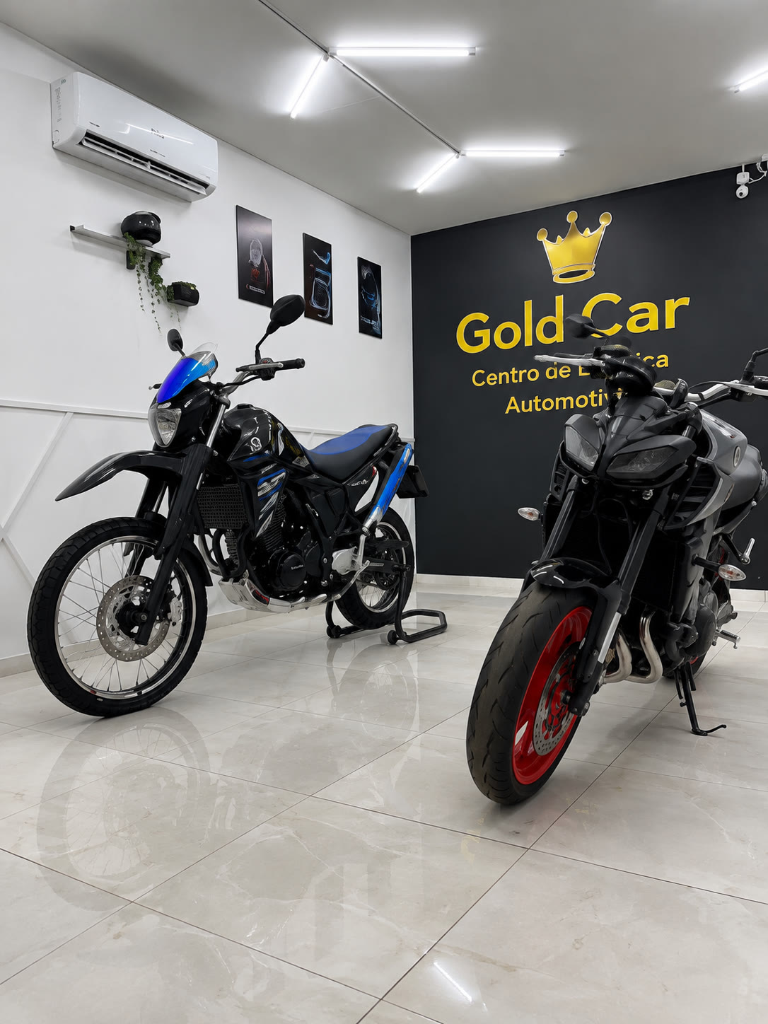 Duas motos no showroom, diante do painel com a marca Gold Car